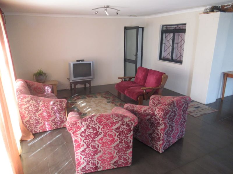 A functional living room featuring tiled flooring, a security gate, and a window fitted with security bars.