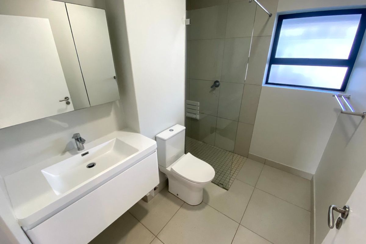 Modern bathroom featuring a wall-mounted vanity, walk-in shower with glass screen, and neutral floor tiles in a clean, contemporary layout.