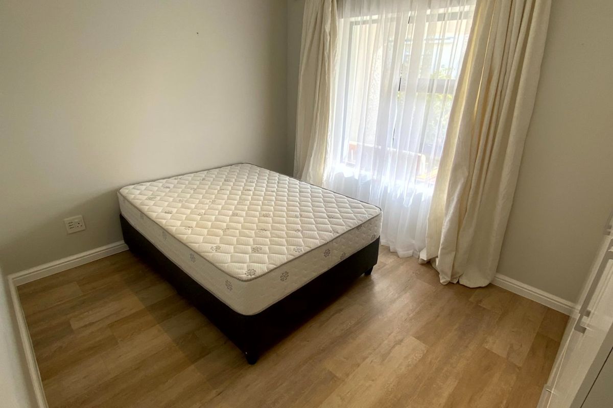 A bright bedroom featuring light-toned laminate flooring and a built-in cupboard, offering a clean and neutral space ready for personalization.