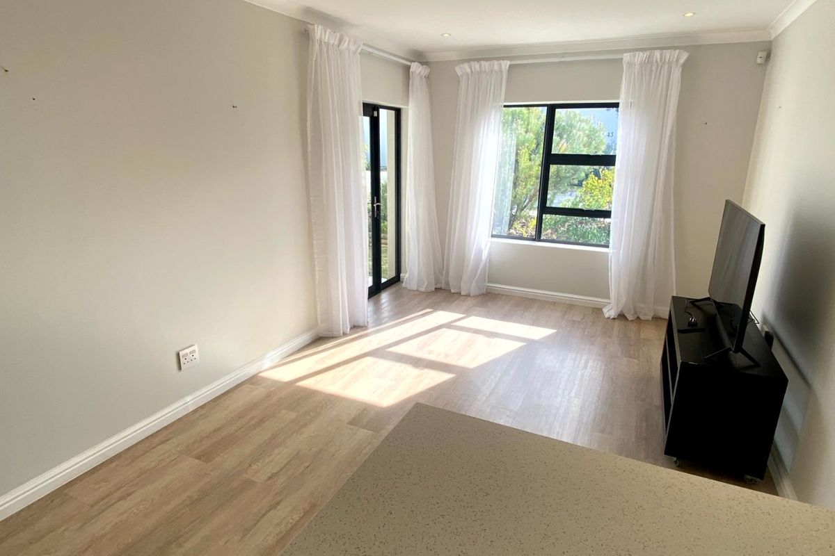 Bright open-plan living area featuring modern laminate flooring, recessed lighting, and large windows with access to an outdoor space.
