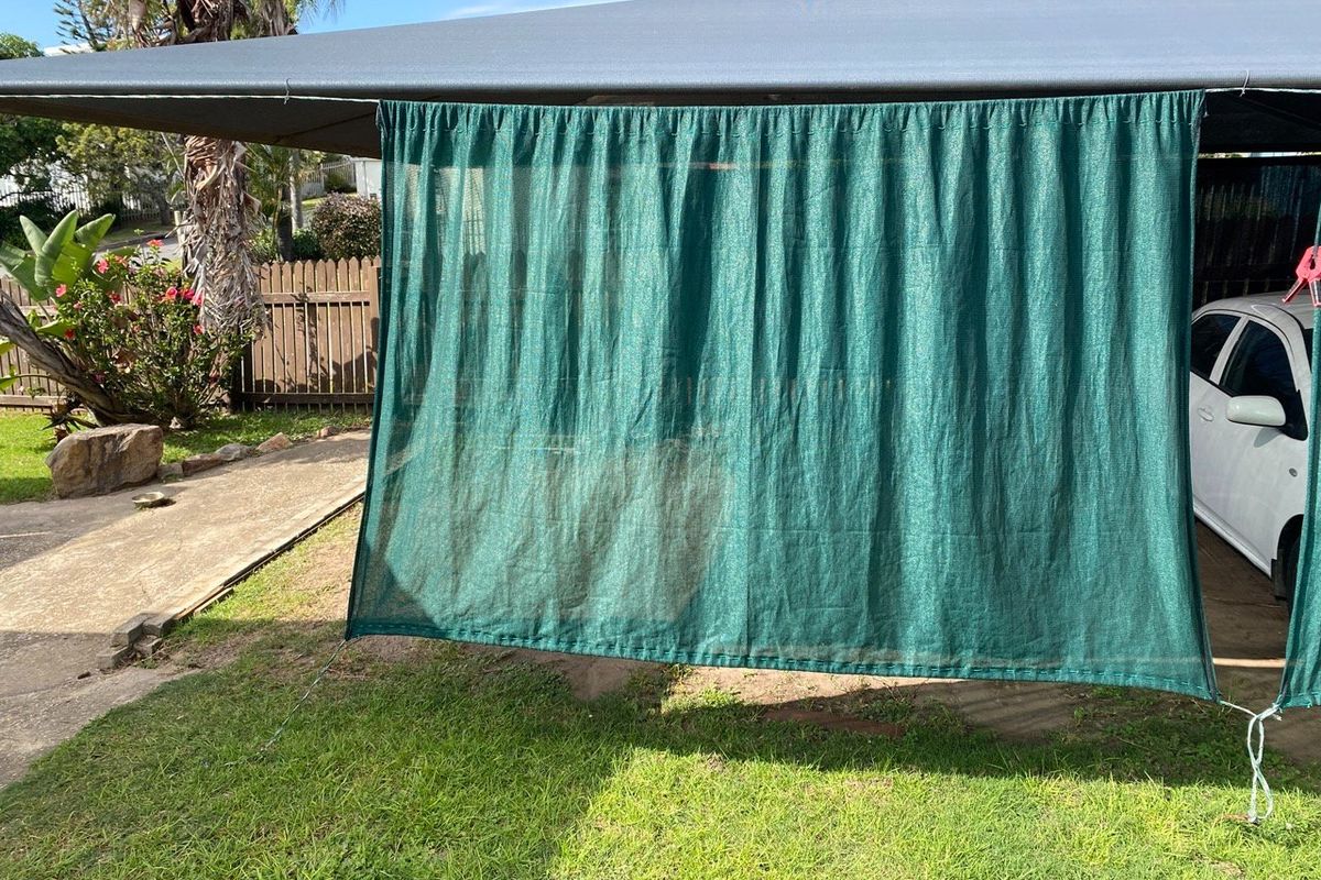 A backyard area featuring a carport structure with green shade cloth screening and a timber boundary fence.