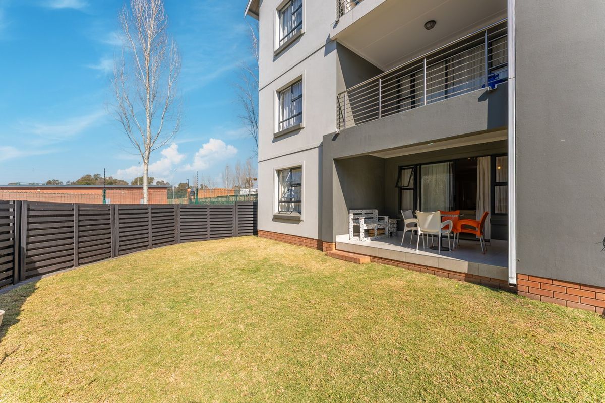 Rear view of the townhouse featuring a private garden, a covered tiled patio, and a balcony with stainless steel railings.