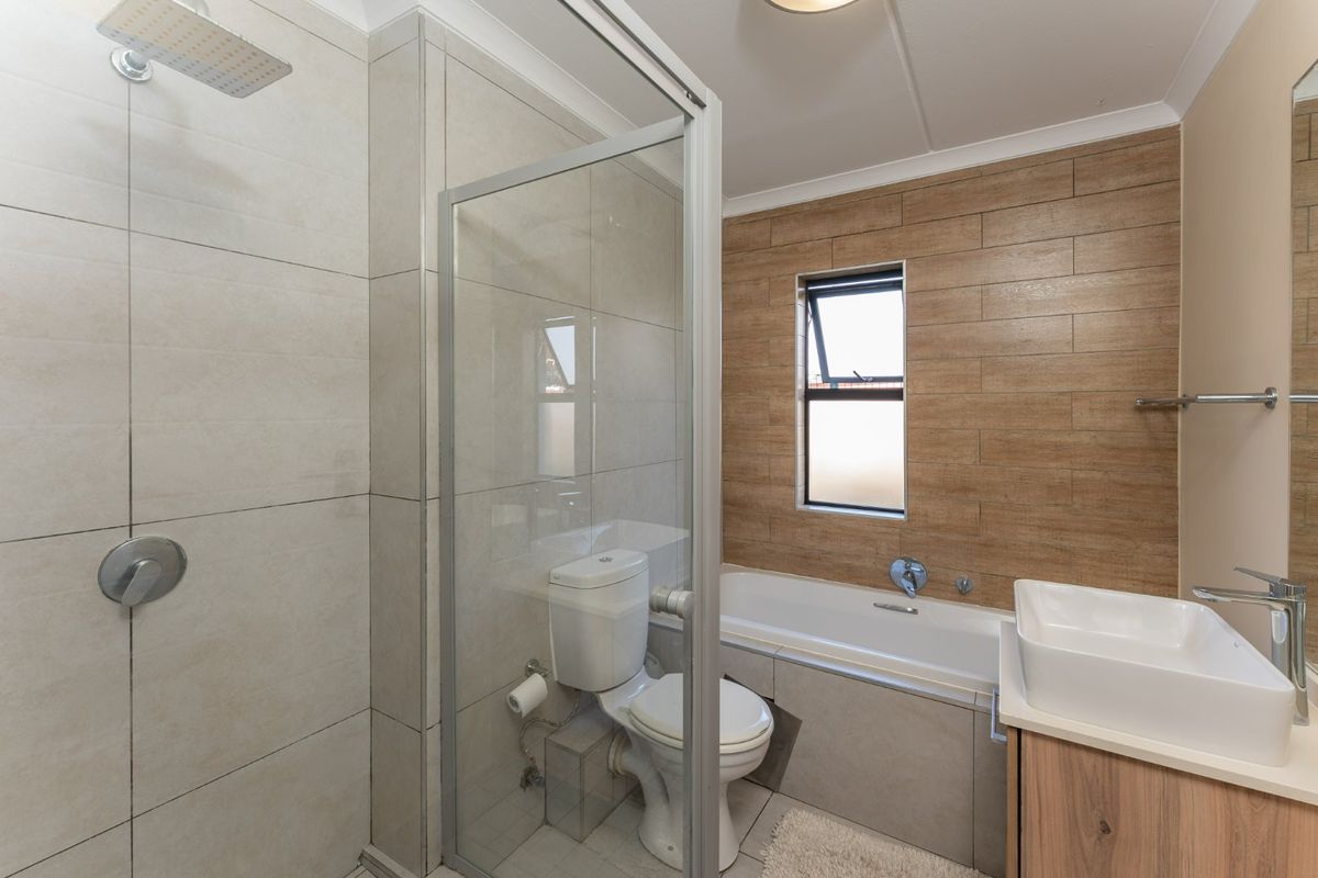 Modern bathroom featuring a glass-enclosed shower, bathtub, vanity basin, and contemporary wall tiling.