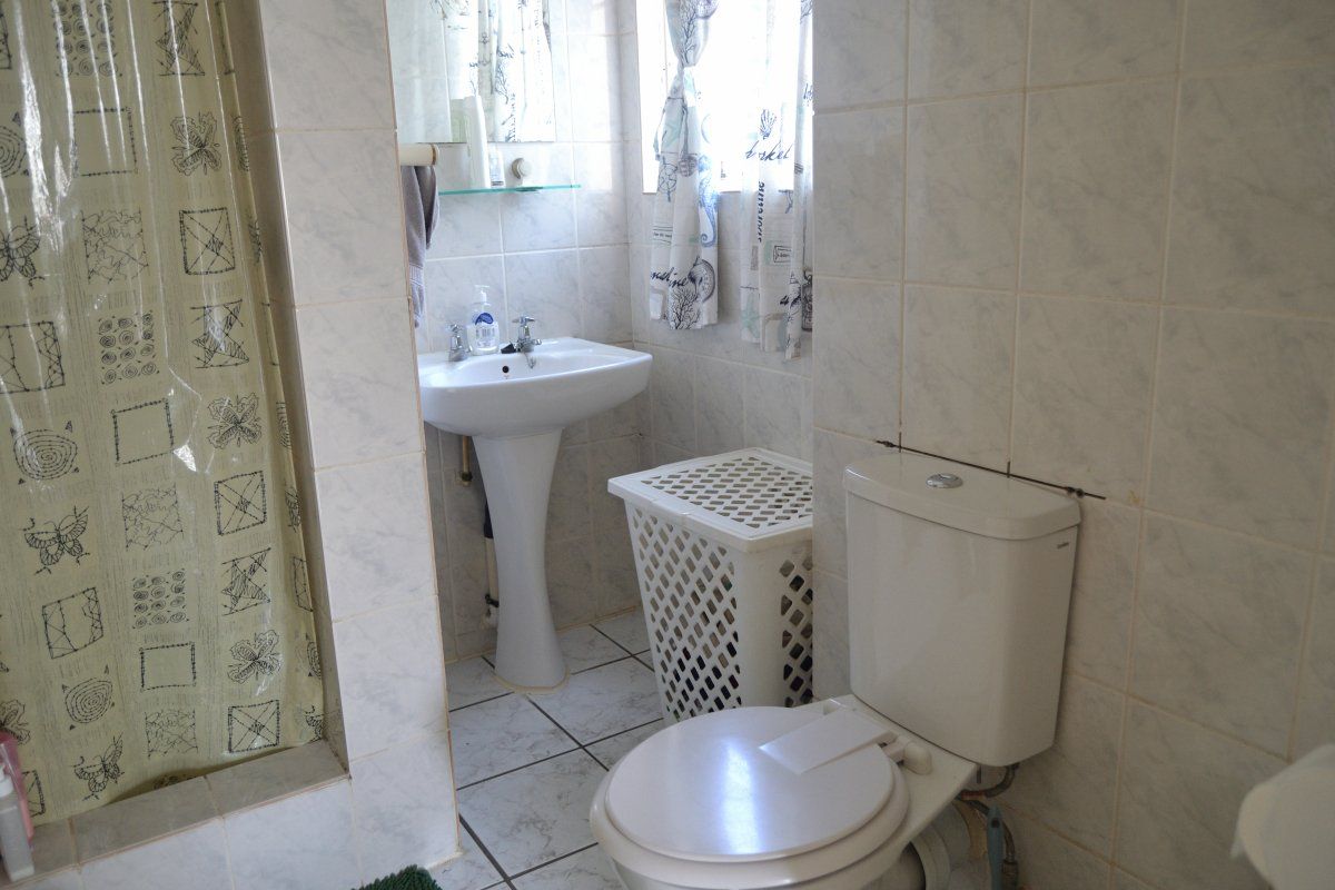 A compact bathroom featuring a pedestal washbasin, toilet, and tiled shower area with dated finishes and visible plumbing.