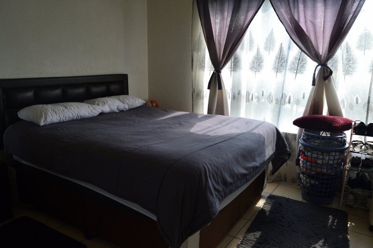 A functional bedroom featuring tiled flooring and large windows with curtain treatments, providing natural light to the space.