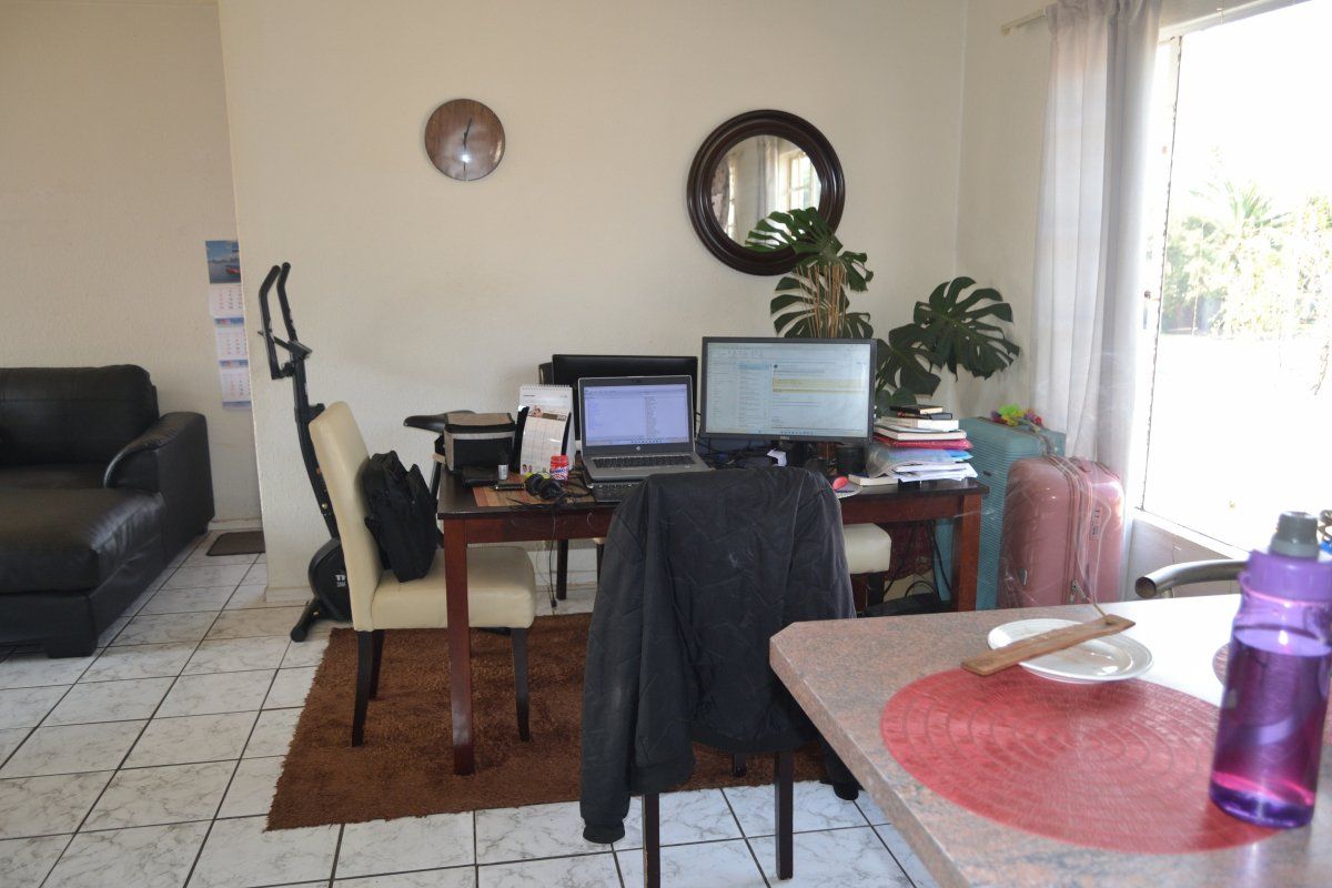 Open plan living area featuring tiled flooring and natural light from a large window, currently utilized as a combined living and workspace.