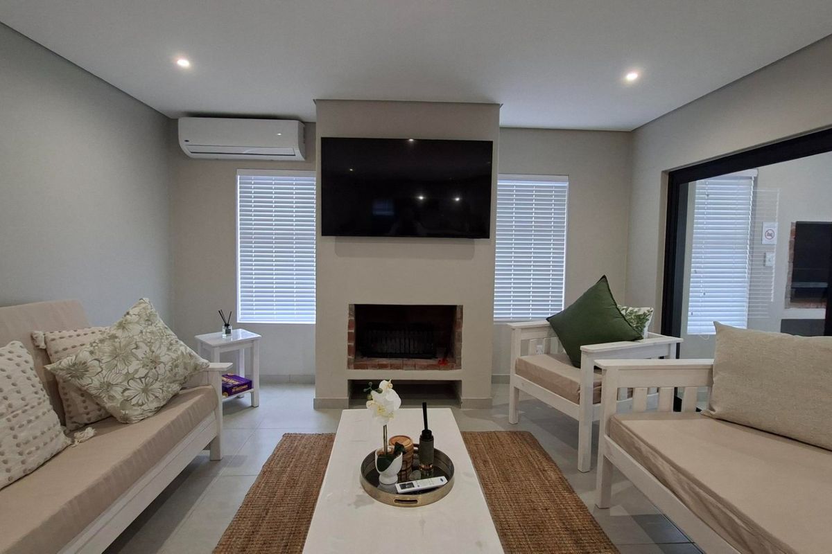 A well-maintained living room featuring a central fireplace, wall-mounted air conditioning, tiled floors, and large sliding glass doors with venetian blinds.