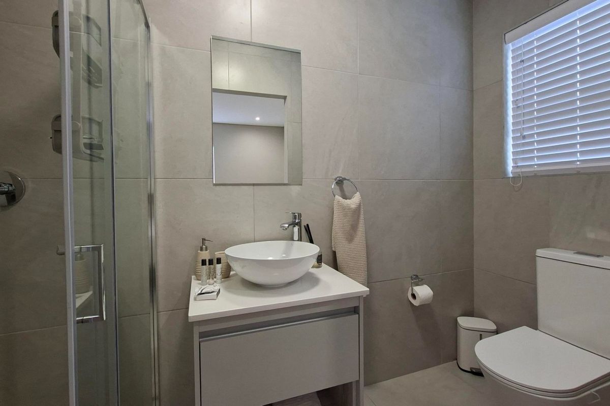 Modern bathroom featuring a glass shower enclosure, vessel sink vanity, and neutral wall tiling.
