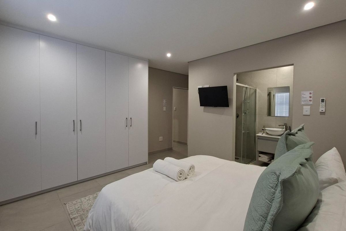 Modern bedroom featuring extensive built-in cupboards, recessed lighting, and a convenient en-suite bathroom with a shower and vanity.