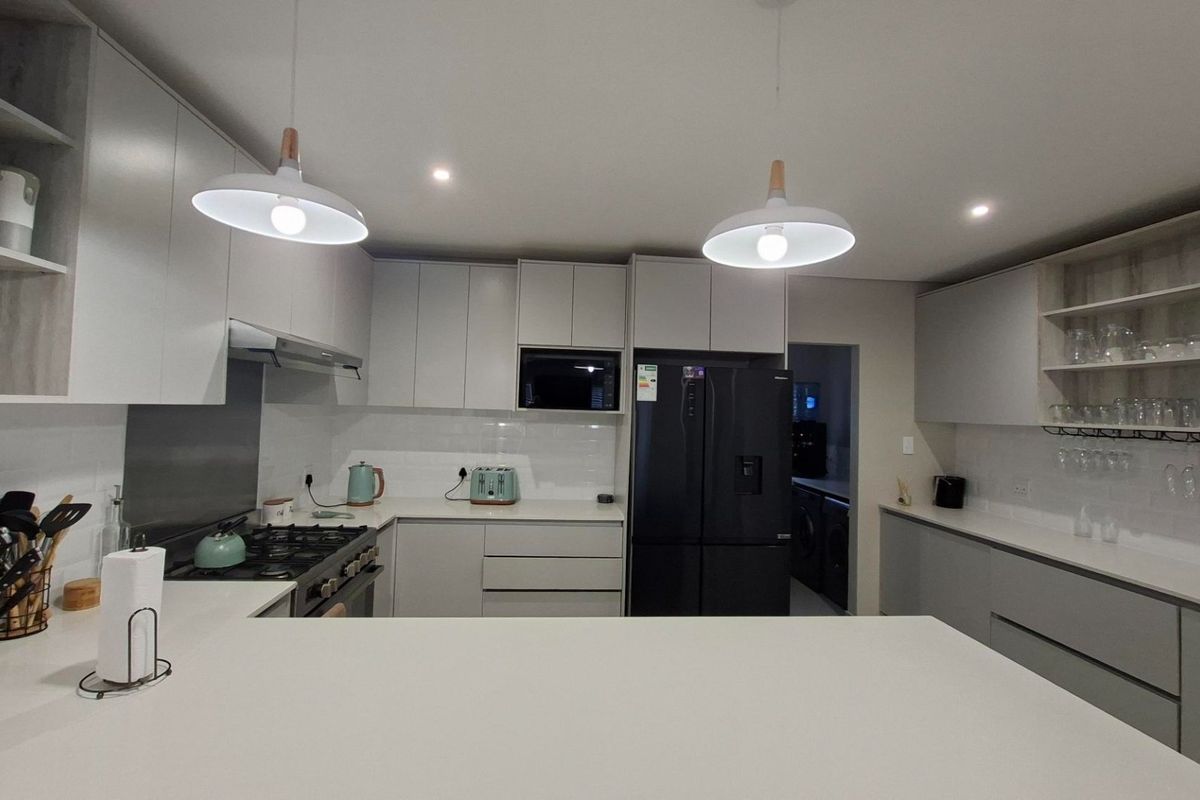 Modern kitchen featuring sleek grey cabinetry, quartz countertops, subway tile backsplash, gas hob, and integrated appliances with contemporary pendant lighting.
