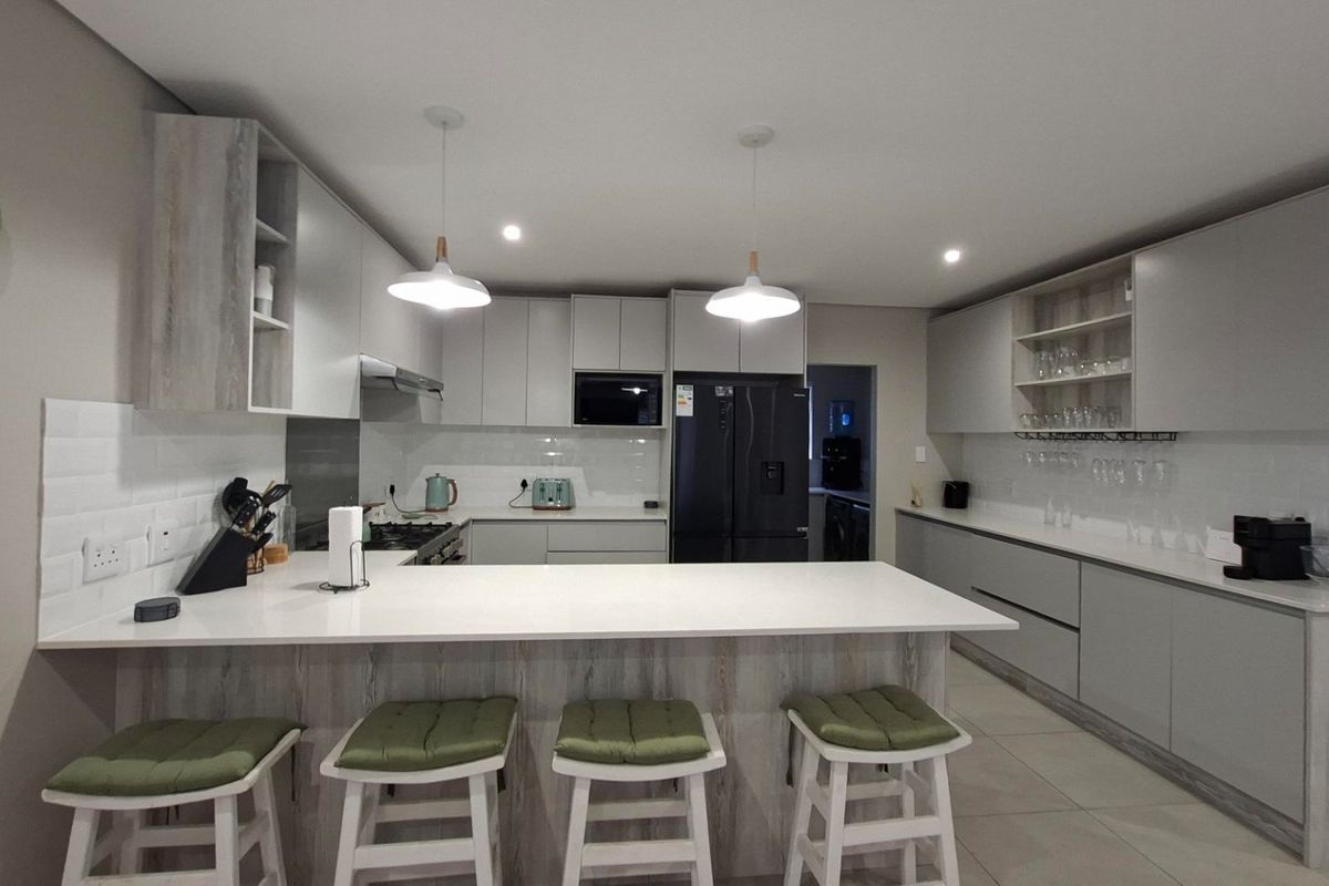 Modern kitchen featuring sleek grey cabinetry, quartz countertops, subway tile backsplash, and integrated appliances with a functional breakfast bar island.