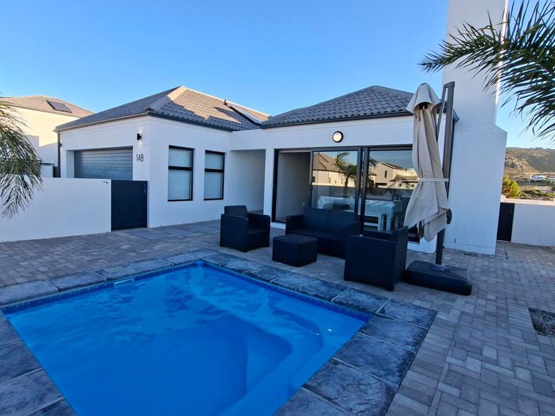 A well-maintained outdoor pool area featuring a paved patio, modern exterior finishes, and direct access to the home through sliding glass doors.