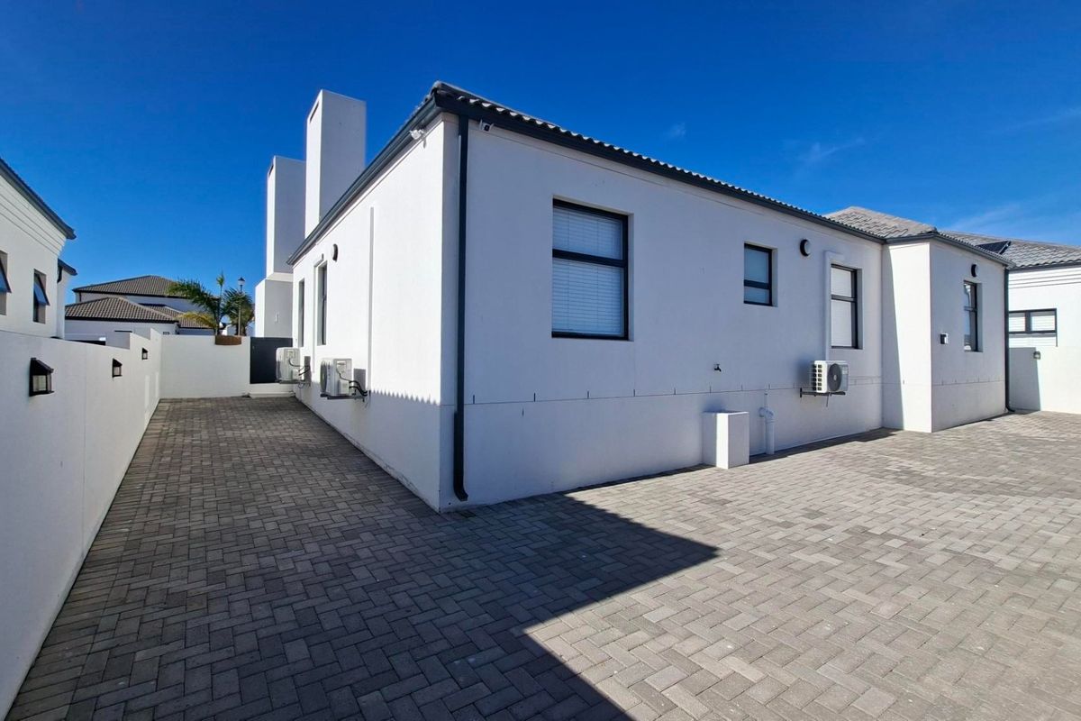 A well-maintained rear exterior view of the property featuring paved driveway, clean white rendered walls, and mounted air conditioning units.