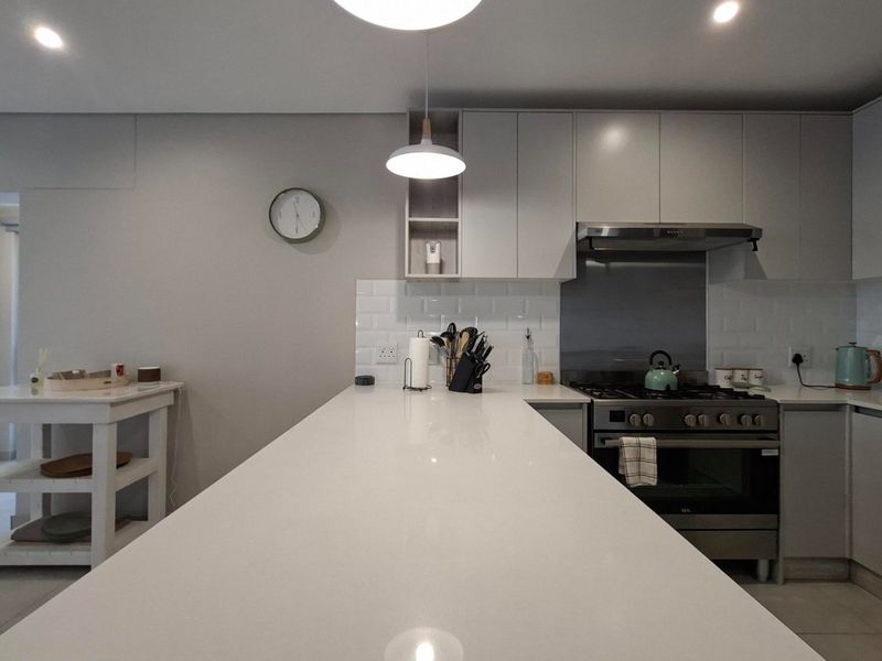 Modern kitchen featuring sleek grey cabinetry, white quartz countertops, subway tile backsplash, and a professional-style gas stove with an integrated extractor fan.