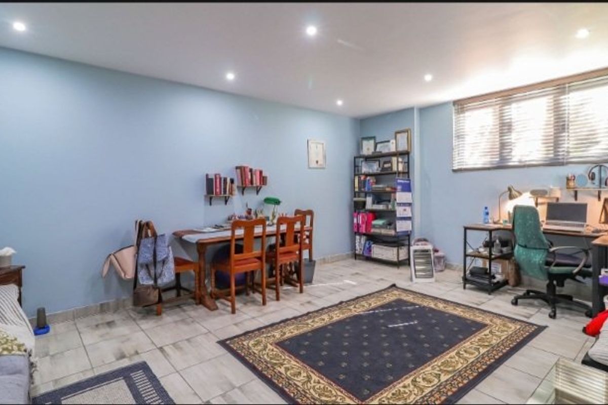 A multi-purpose living space featuring tiled flooring, recessed downlighting, and venetian blinds, currently utilized as a home office and study area.
