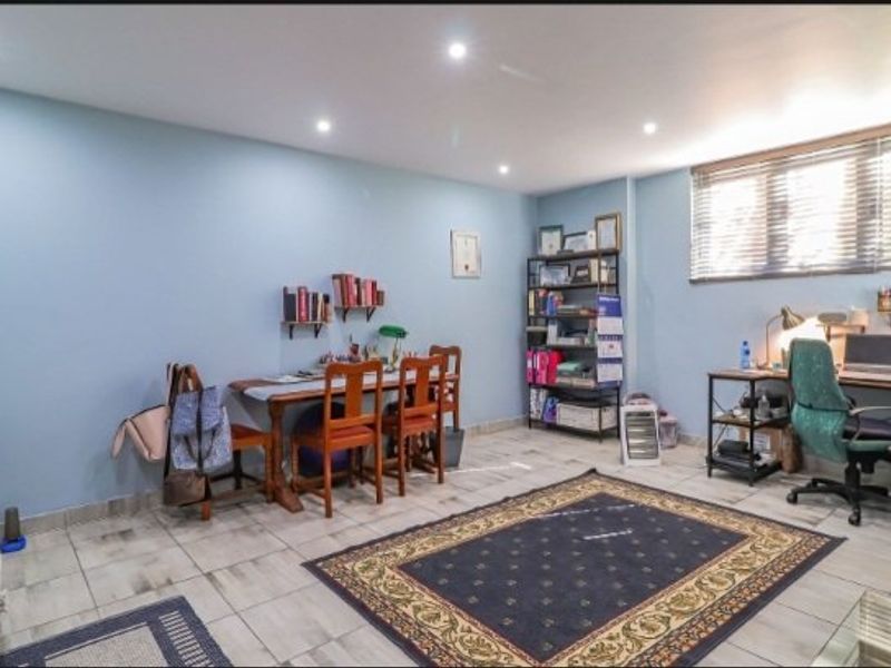 A multi-purpose living space featuring tiled flooring, recessed downlighting, and venetian blinds, currently utilized as a home office and study area.