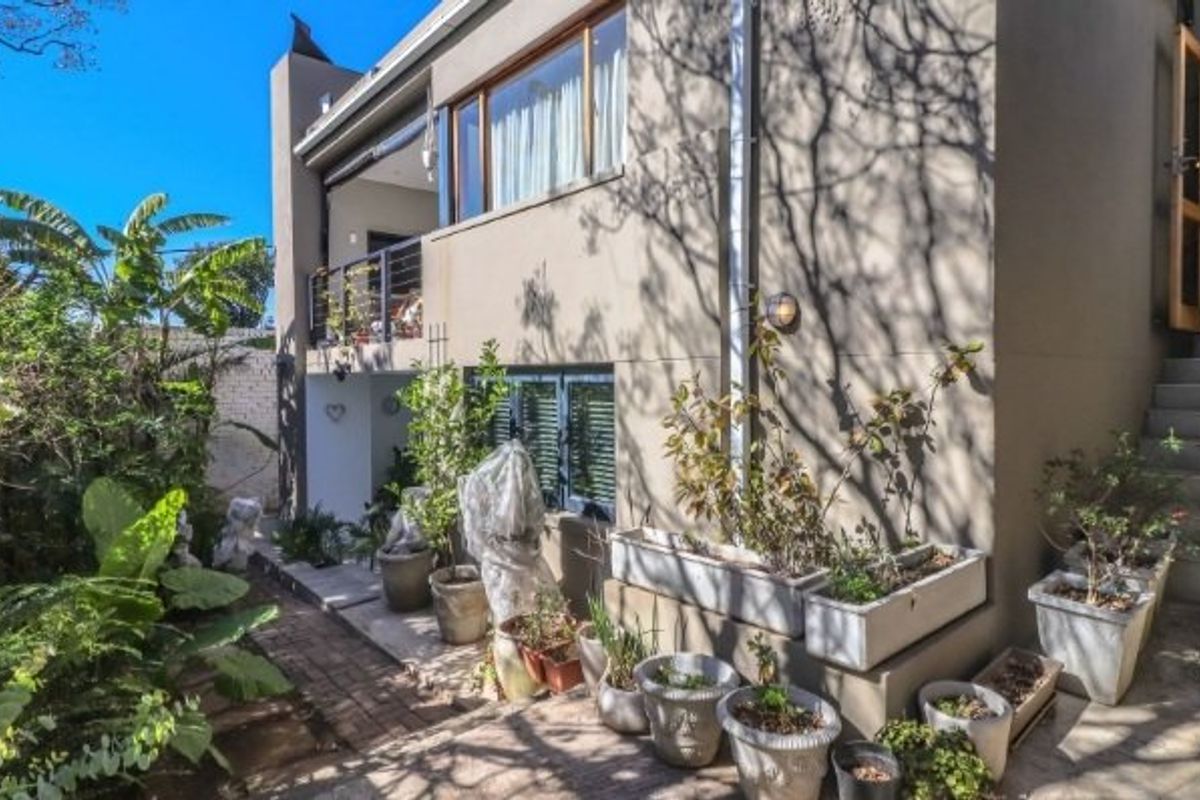 Rear exterior view of the property featuring a balcony, external staircase, and landscaped garden area with paved pathways.