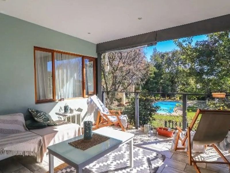 A covered patio area featuring tiled flooring, recessed lighting, and a metal balustrade, offering a pleasant view of the garden and swimming pool.