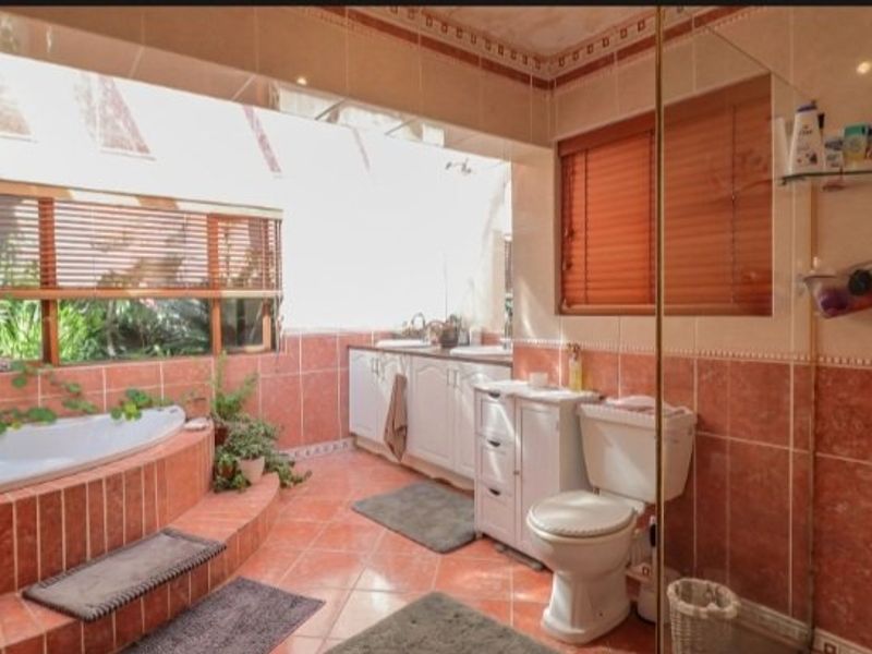 Spacious bathroom featuring a corner bathtub, dual vanity basins, and floor-to-ceiling tiling with a large window providing natural light.