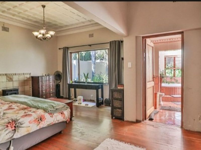 Spacious bedroom featuring hardwood flooring, a decorative coffered ceiling, and direct access to an en-suite bathroom with built-in storage.