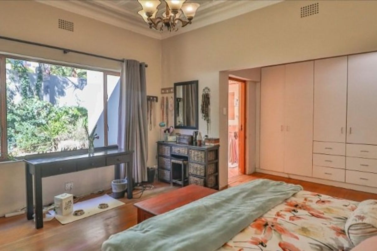 Spacious bedroom featuring hardwood flooring, extensive built-in cupboard storage, and a large window overlooking the garden.