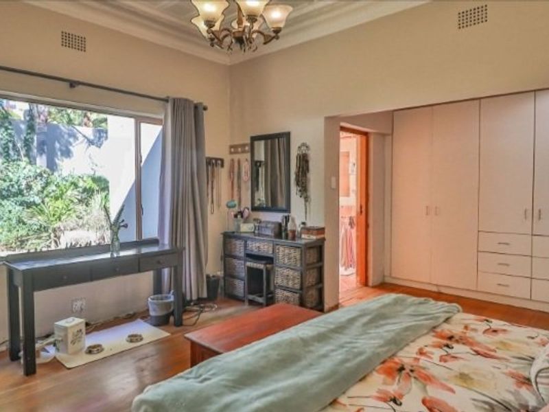 Spacious bedroom featuring hardwood flooring, extensive built-in cupboard storage, and a large window overlooking the garden.