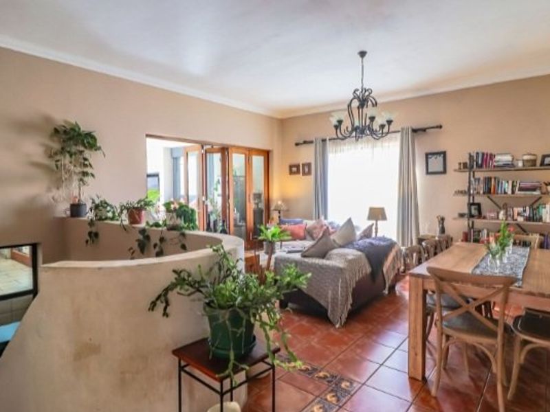 Spacious open-plan living and dining area featuring terracotta floor tiles, a decorative wrought iron chandelier, and access to an adjoining space via bi-fold doors.