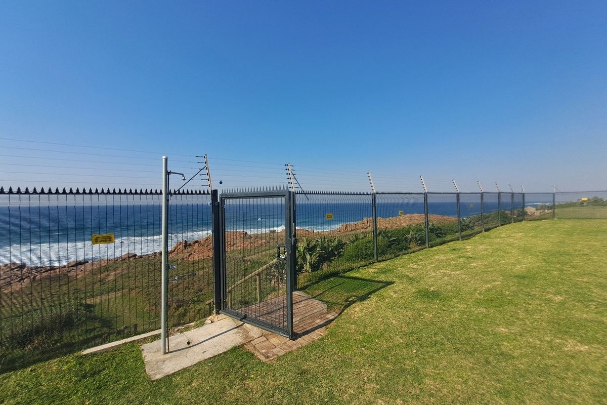 Rear garden area featuring secure perimeter fencing with electric wires, a pedestrian gate, and an outdoor shower overlooking the ocean.