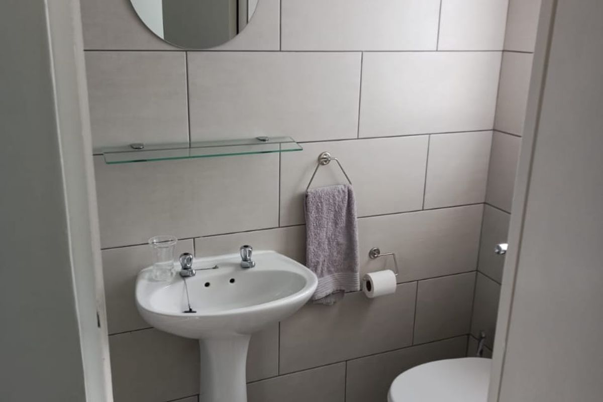 A compact, modern bathroom featuring neutral wall tiles, a pedestal basin, and a standard toilet.