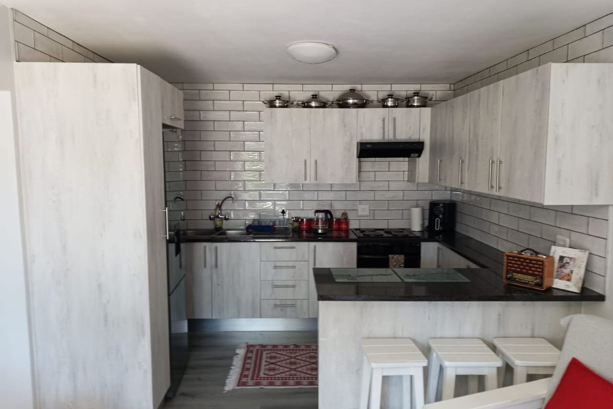 Modern kitchen featuring light wood-grain cabinetry, dark stone countertops, a subway tile backsplash, and a functional breakfast bar area.