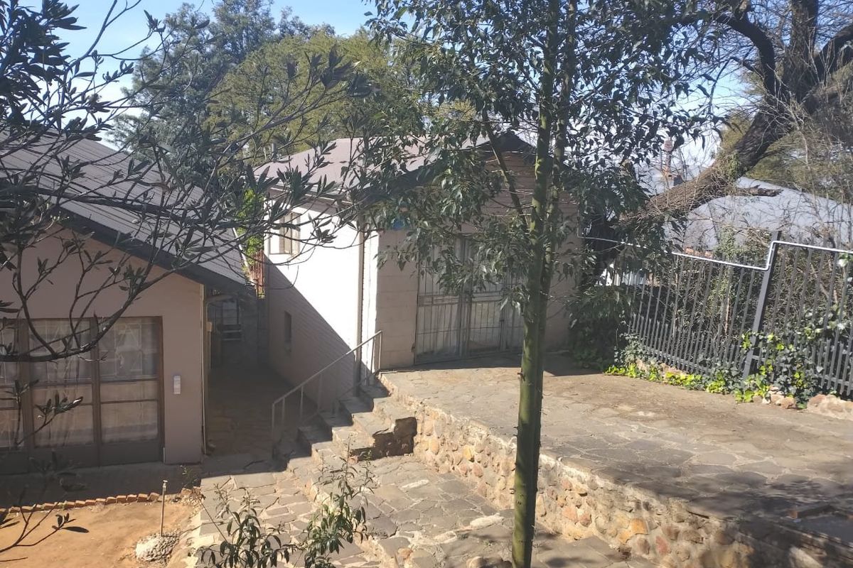 Rear exterior view featuring a stone-paved patio area, retaining wall, and metal security fencing leading to the building entrance.