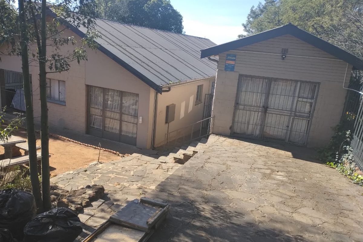 Rear view of the property featuring a stone paved driveway, metal roofing, and secure access points with security gates.