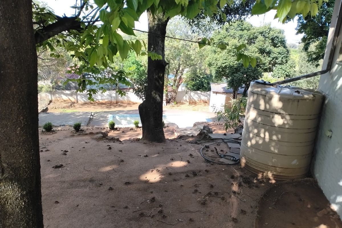 A view of the rear garden featuring a large water storage tank, a swimming pool, and established trees with a boundary wall.