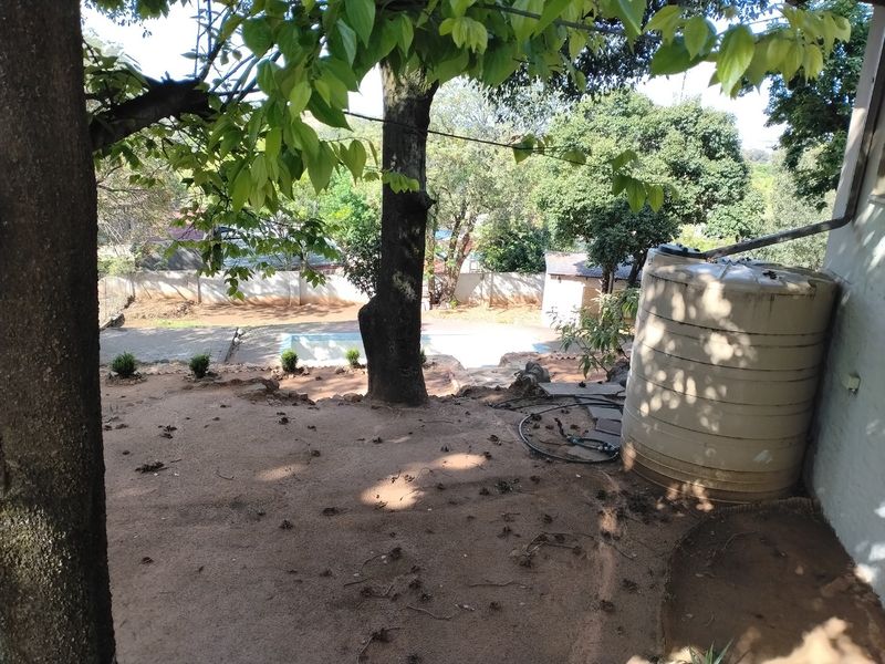 A view of the rear garden featuring a large water storage tank, a swimming pool, and established trees with a boundary wall.