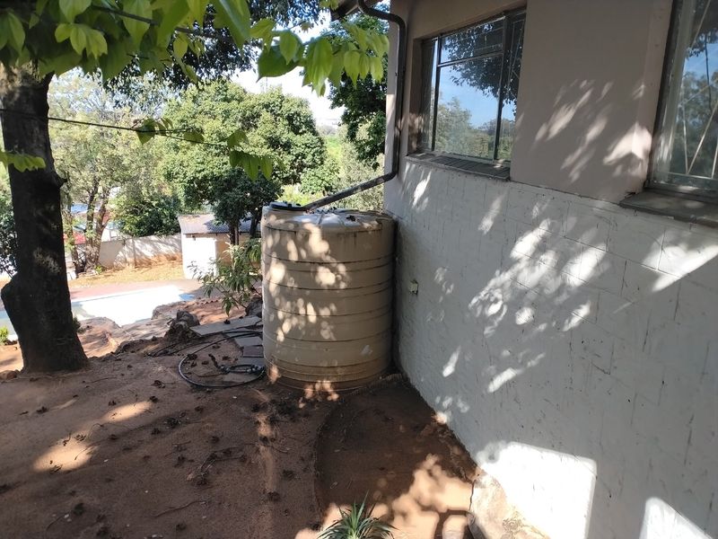 Rear exterior view showing a water storage tank connected to a downpipe against a painted brick wall with metal window frames.