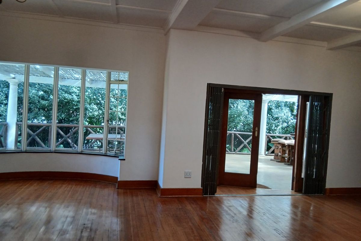 Spacious living area featuring polished hardwood floors, a coffered ceiling, a large bay window, and folding doors opening onto an outdoor patio.