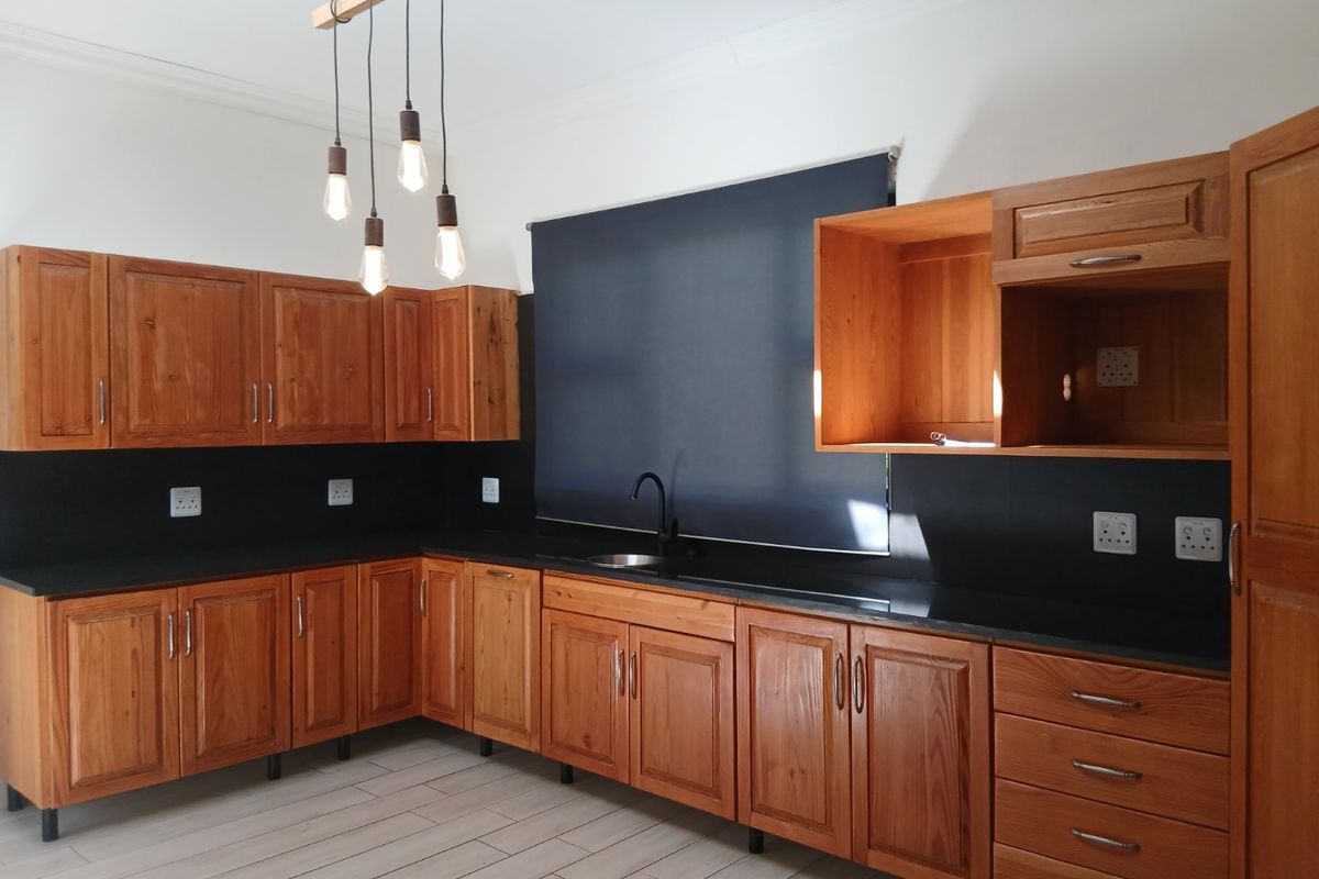 A clean, modern kitchen featuring warm wooden cabinetry, contrasting black countertops, a sleek undermount sink, and stylish pendant lighting.