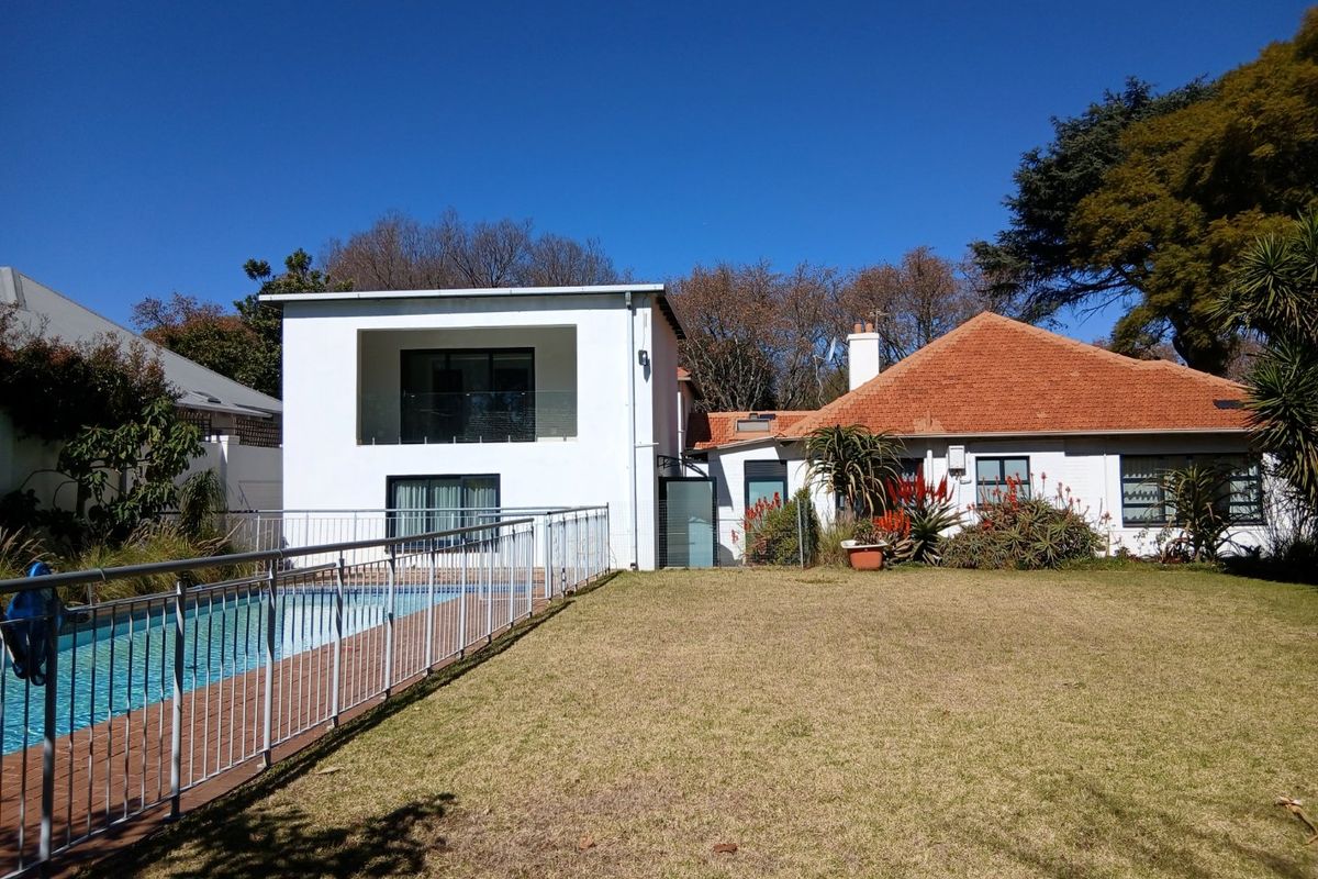 Rear view of the property featuring a swimming pool with safety fencing, a landscaped lawn, and a modern two-story extension alongside the original structure.