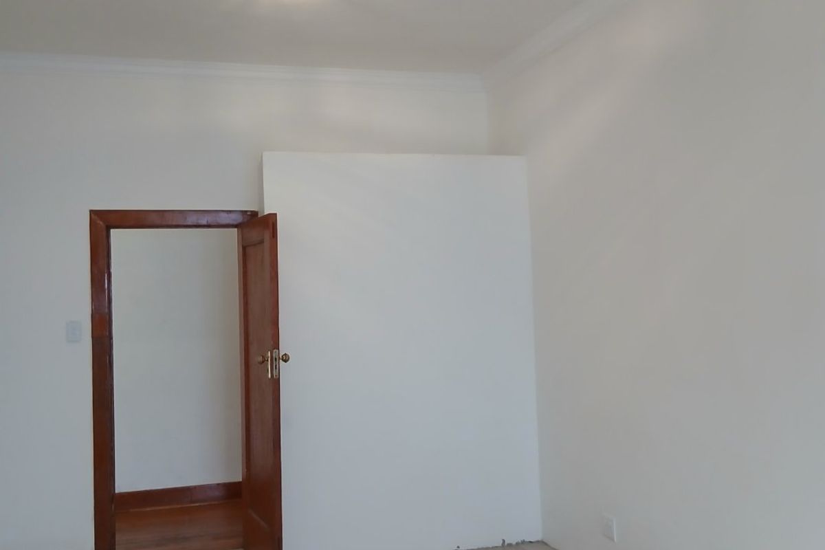 An empty bedroom featuring light-toned tiled flooring, white walls with coving, and a wooden door frame leading to an adjacent space.