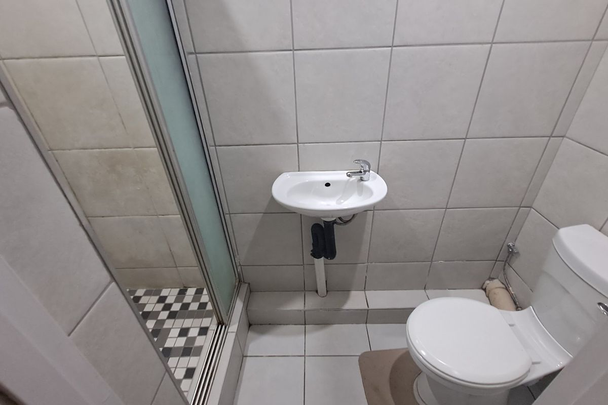 A compact bathroom featuring a shower enclosure, wall-mounted basin, and toilet with neutral ceramic tiling throughout.