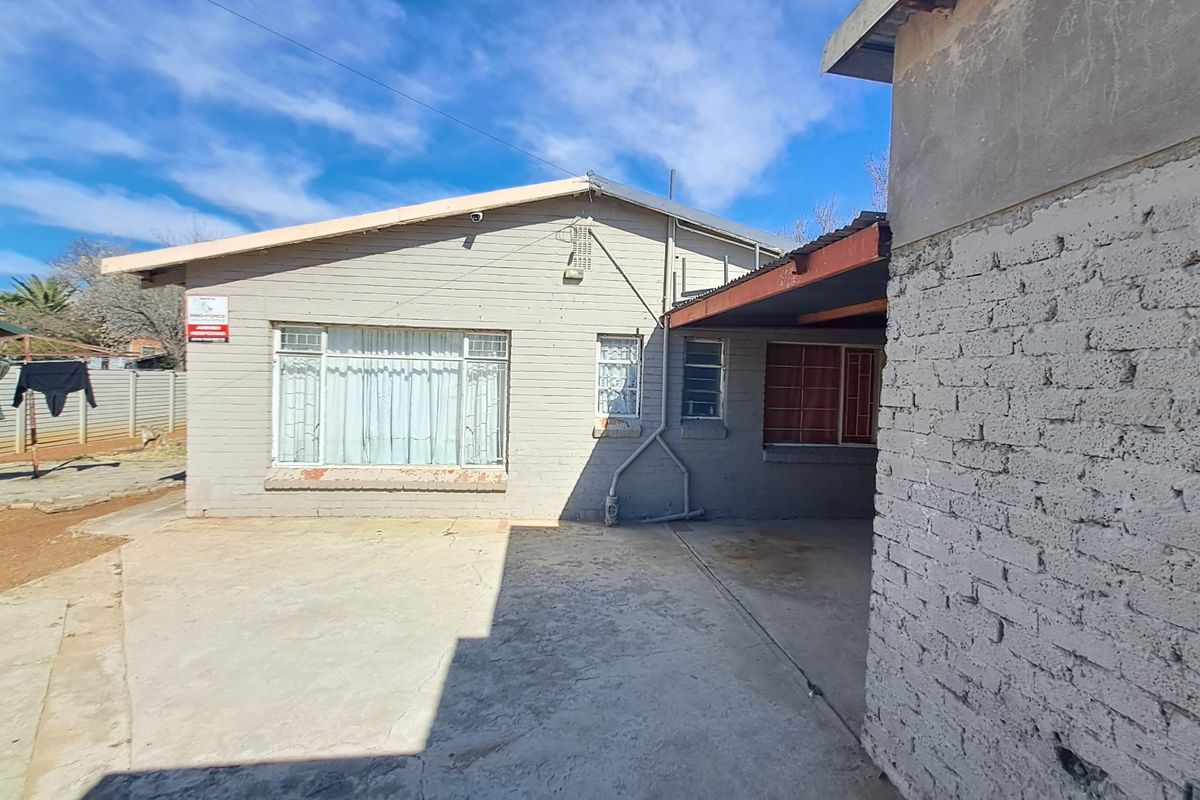 Rear view of the property featuring a concrete driveway, covered patio area, and painted brick exterior walls with security bars on windows.