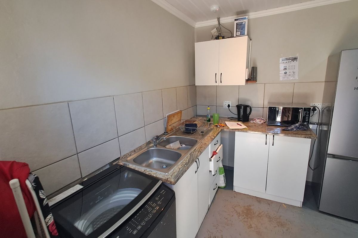 A compact kitchen area featuring granite countertops, tiled backsplash, and functional cabinetry, requiring some cosmetic updates to the flooring and finishes.