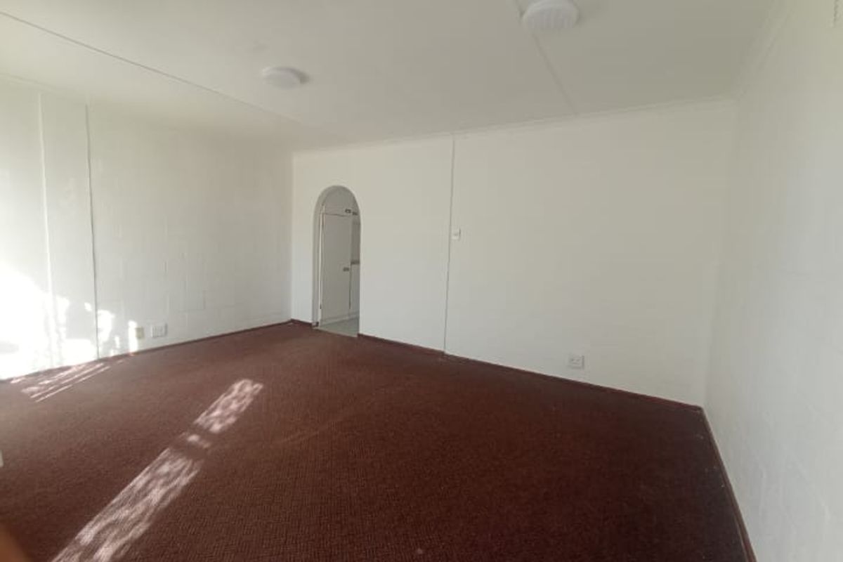 A spacious, empty living room featuring neutral walls, carpeted flooring, and a distinctive arched doorway leading to an adjacent area.
