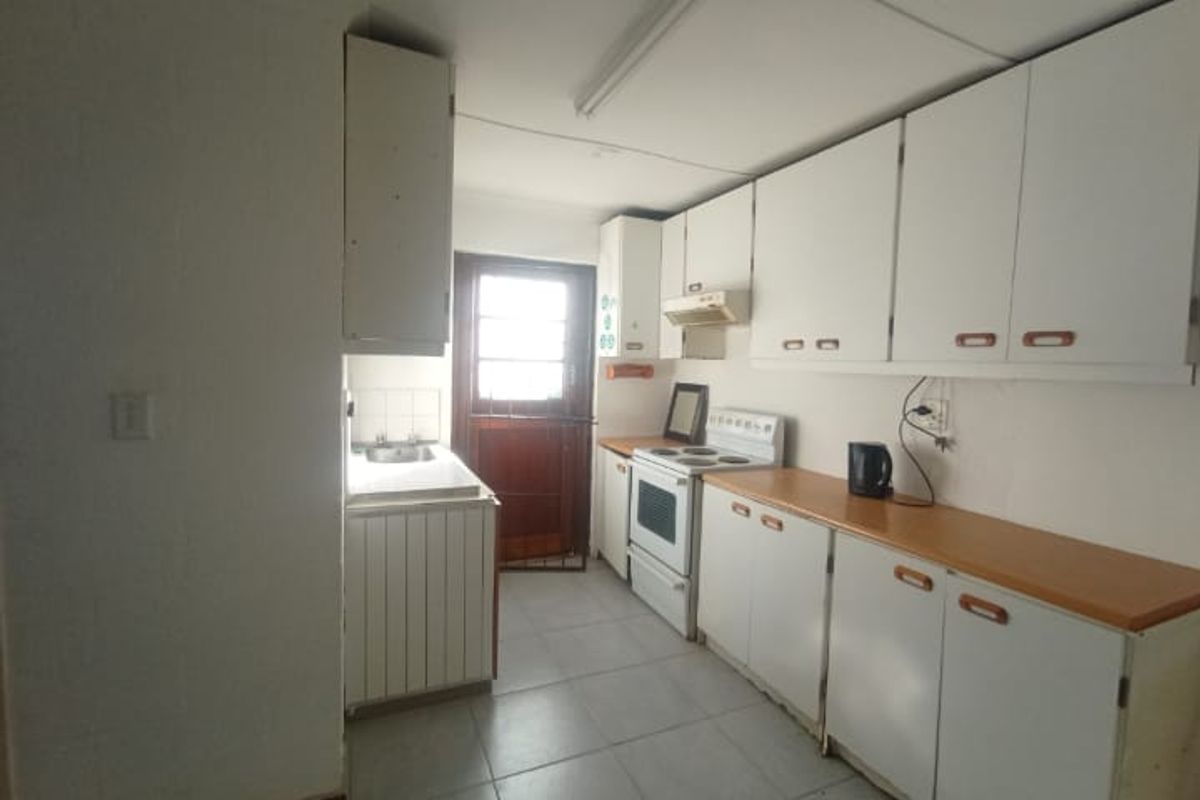 A functional kitchen featuring white cabinetry, laminate countertops, a freestanding stove, and tiled flooring, offering potential for modernization and cosmetic updates.