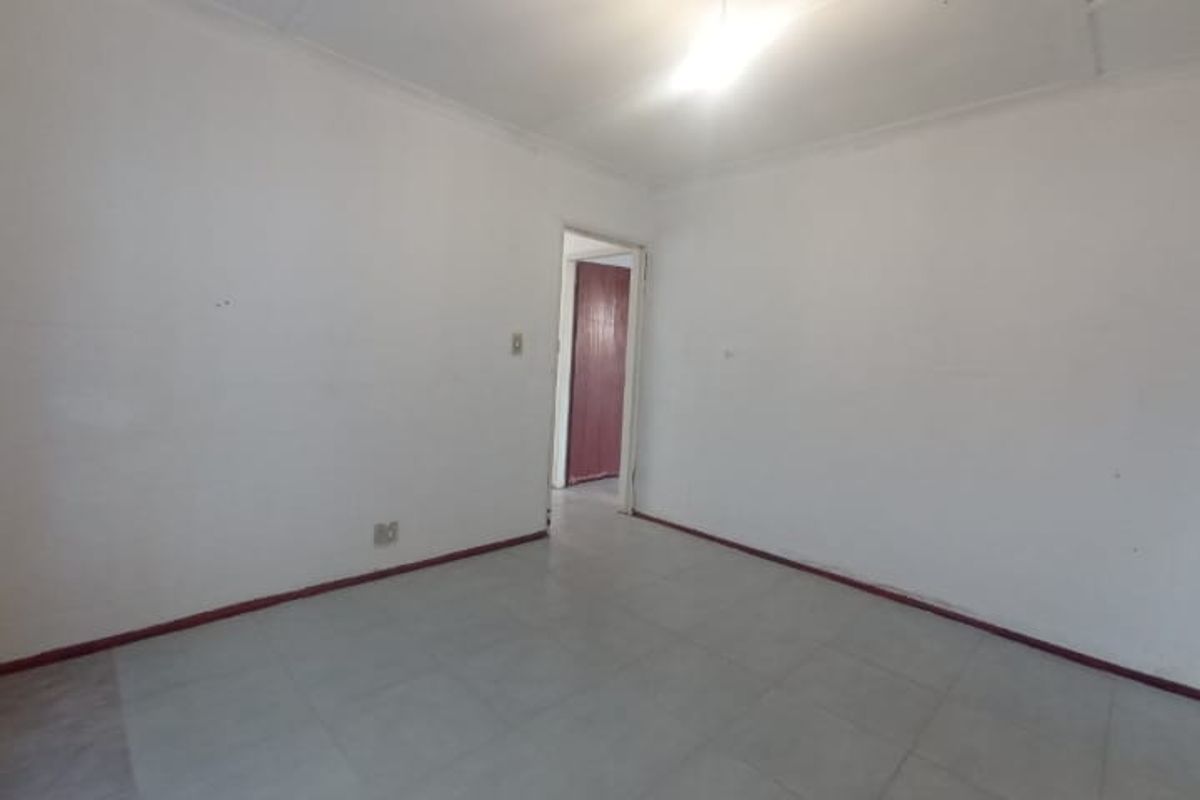 An empty, neutrally painted living area featuring tiled flooring and basic ceiling lighting, providing a blank canvas for potential interior design updates.