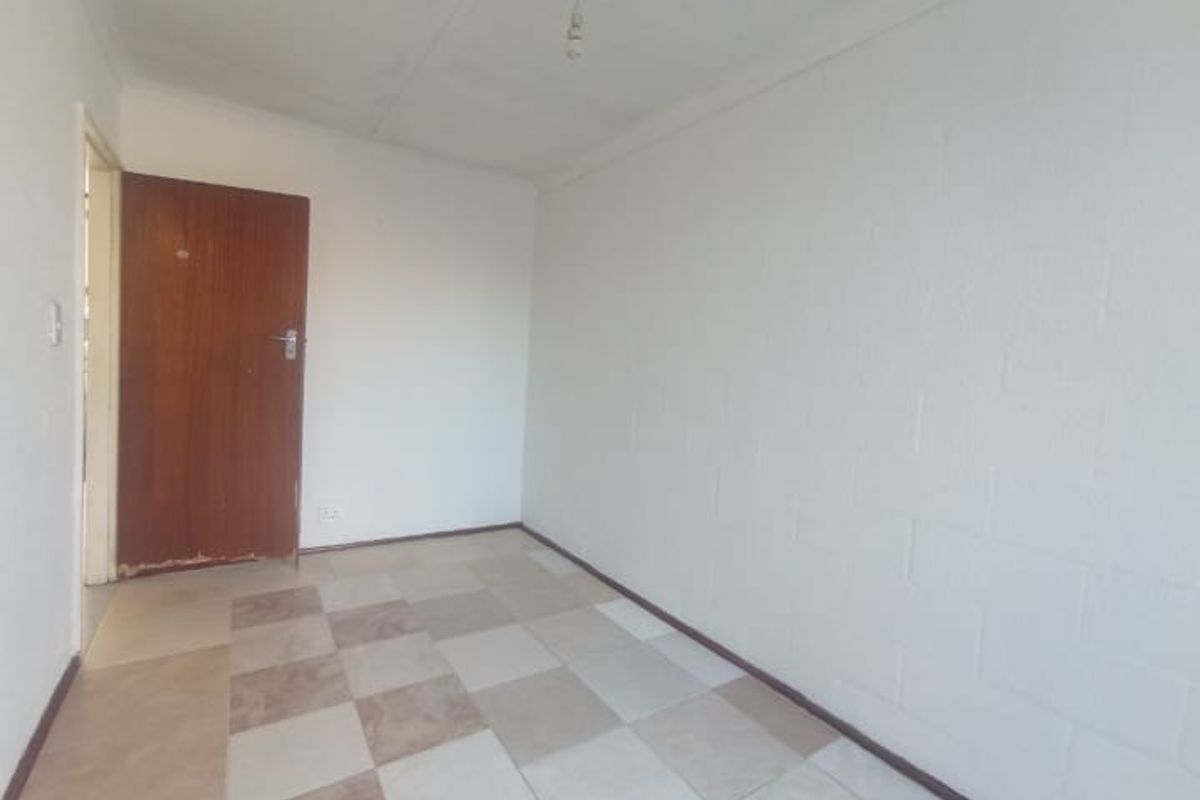 An empty, basic bedroom featuring tiled flooring and a standard timber door, requiring cosmetic updates to improve its overall appeal.