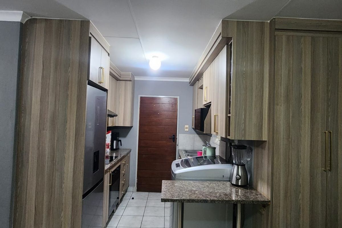 A compact kitchen featuring modern wood-look cabinetry, granite countertops, tiled flooring, and a built-in pantry cupboard.