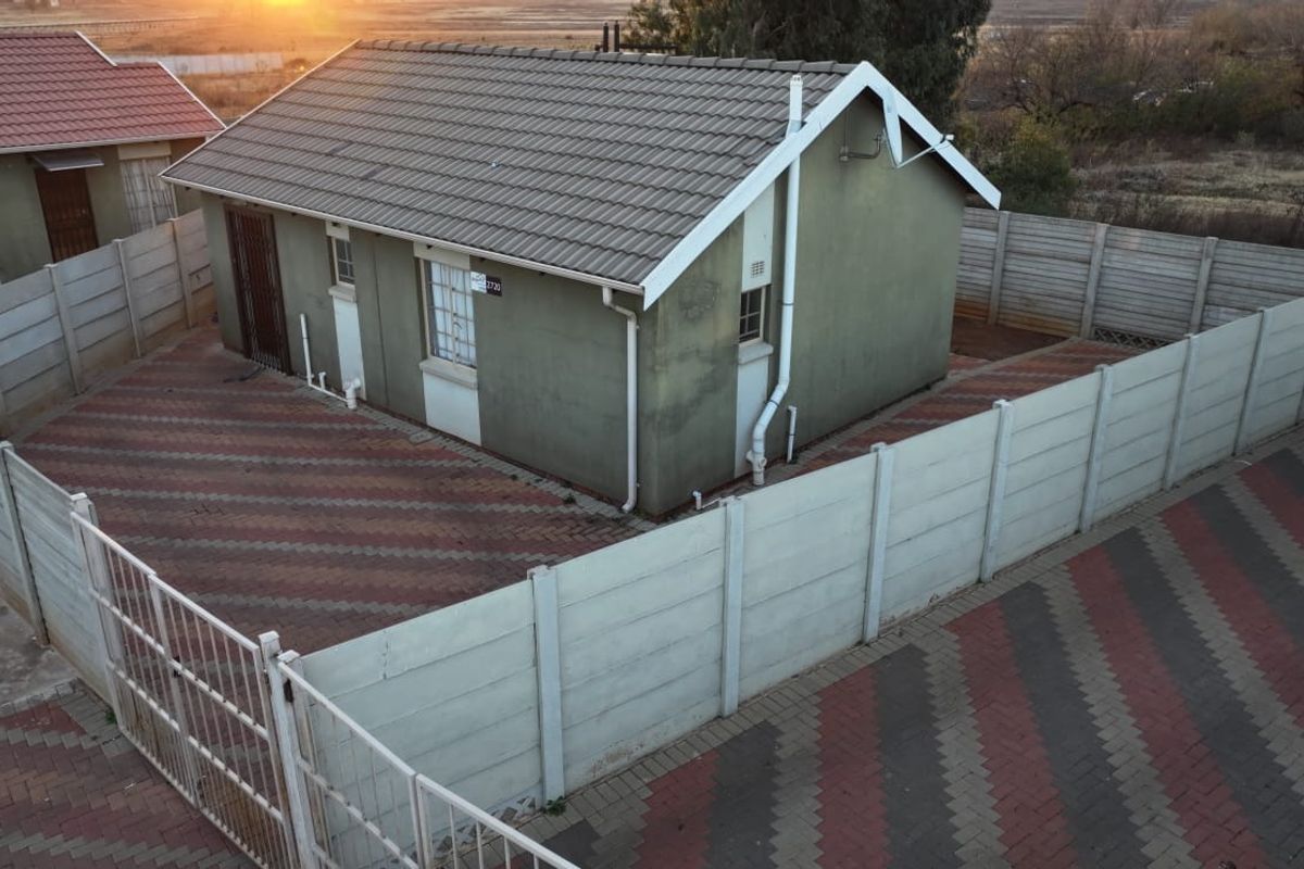 An elevated view of the rear exterior of the house, featuring a tiled roof, paved yard, and secure precast concrete boundary walling.