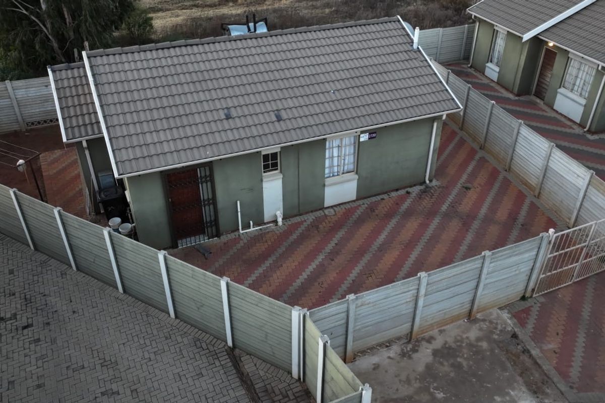 Aerial view of a detached house featuring a tiled roof, paved driveway, and enclosed by precast concrete boundary walls.