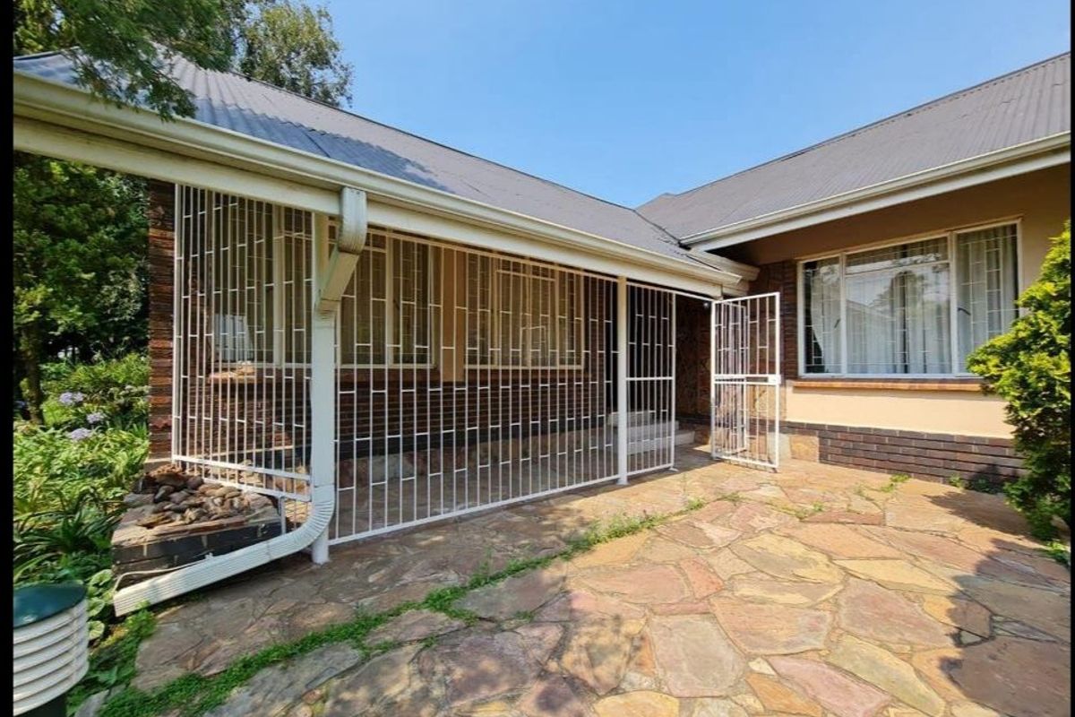 A rear exterior view of the house featuring a stone-paved patio area, secure metal gates, and brick wall finishes.